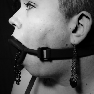 A black and white picture of a white person's profile, showing off the gag's mouthpiece and strap.