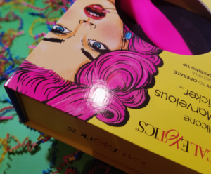 A close-up of the corner of the Marvelous Flicker's box. It's an upside down view of the art pop femme and her curly pink hair.