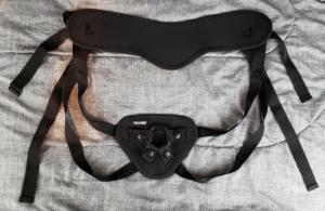 A double leg strap style strap-on harness in black neoprene sprawled on a dark gray background.