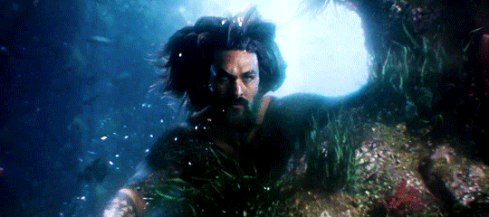 A gif of Jason Momoa as Arthur Curry, hair fanned out as he hovers in the water and peers past the camera.