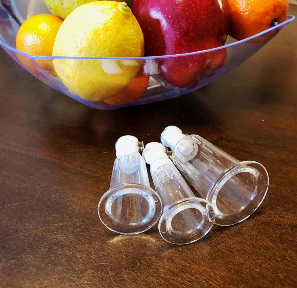 A close-up of the three clear acrylic cylinders laying on their sides with their open cups facing outward. The fruit bowl is behind them.