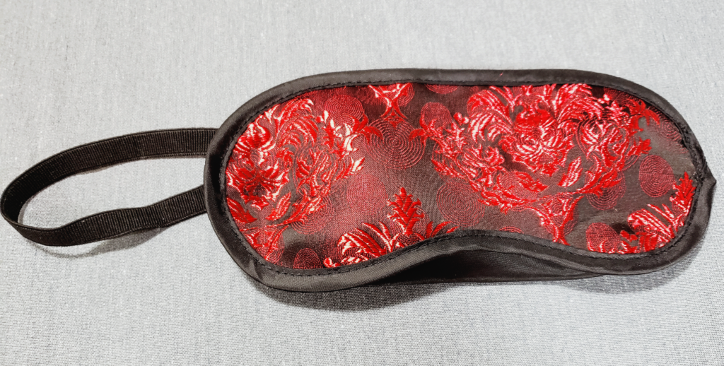 A fabric blindfold with black lining and an elastic strap.