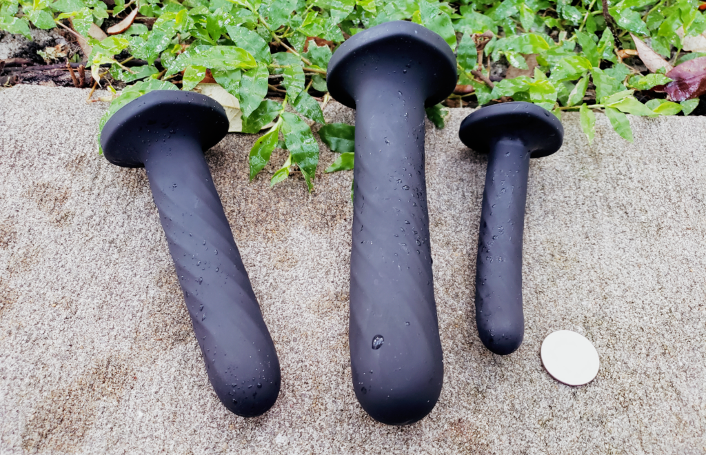 The Twist dildos fanned out on their sides with a quarter laying beside them for size comparison.