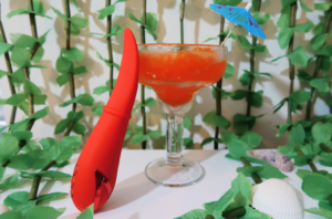The Laguna Beach Lover sex toy posed against a glass with a mini umbrella in it. The Laguna Beach Lover is a vibrator with a tongue-shaped appendage on a handle.
