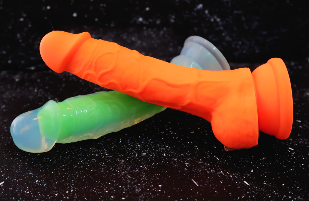 The orange Neo Elite 7.5 Inch with Balls laying on top of the Neo Elite Glow 7.5 Inch with balls.