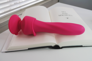 The Wall Banger Deluxe Vibrator laying across an open book.