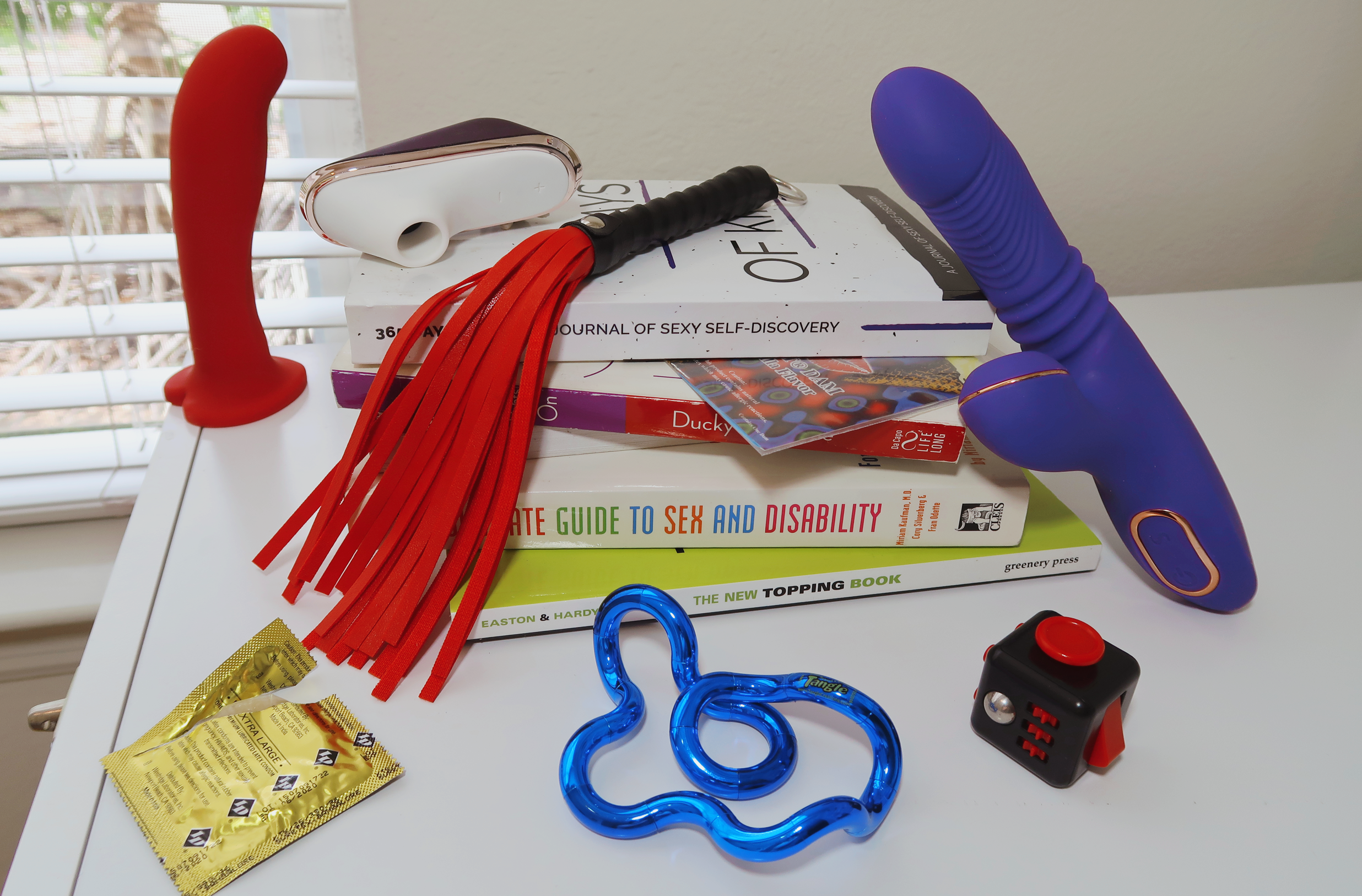 A pile of books surrounded by several sex toys and stim toys.