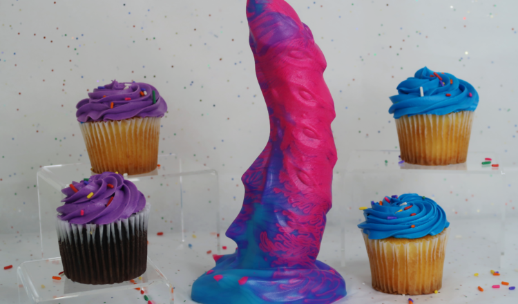 A neon-colored dragon themed dildo surrounded by cupcakes.