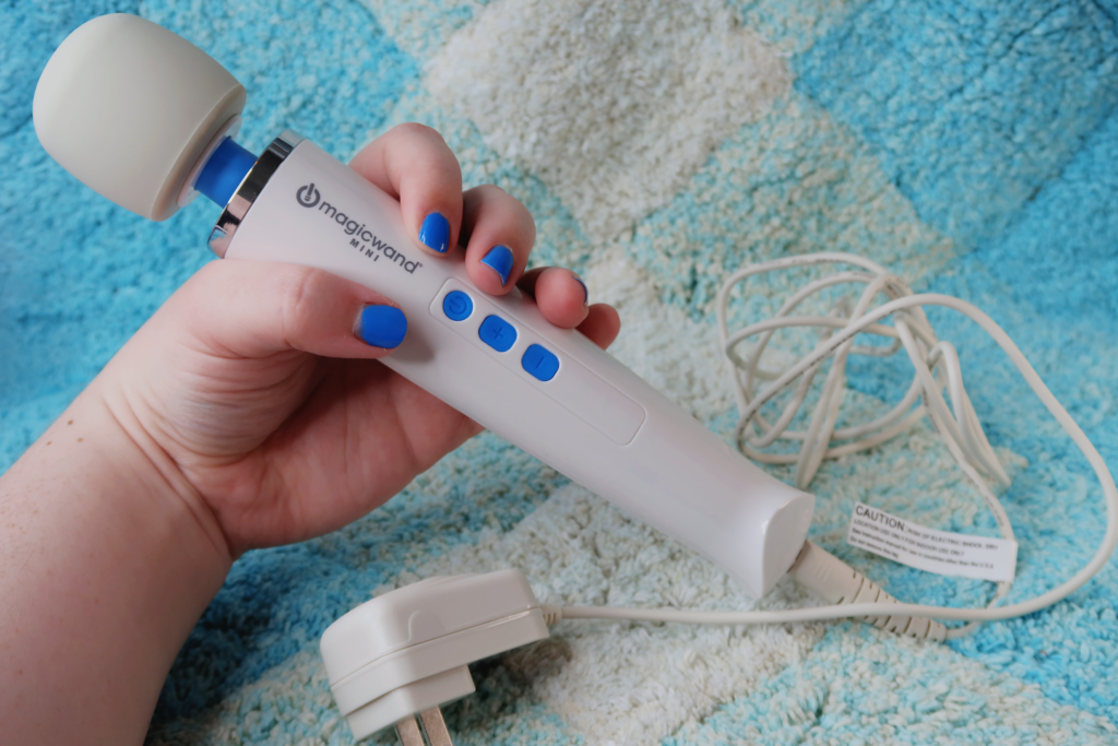 A white person's hand holding the Mini Magic Wand, showing off its charge cord.