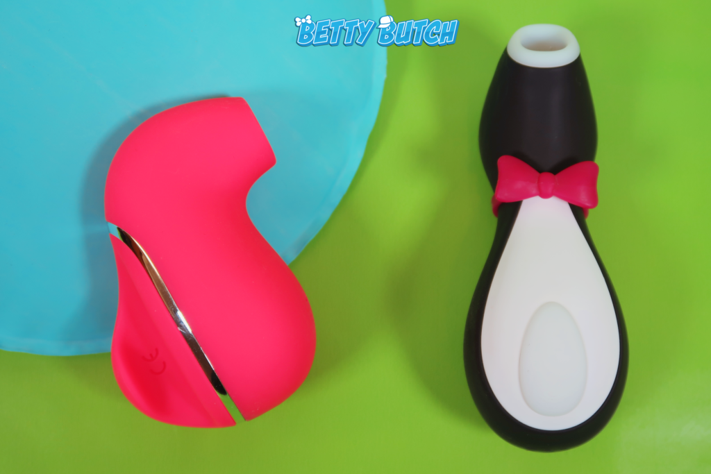 A comparison shot of the Suki and Penguin air pulsation toys. They're laying against a bright green background with an odd blue cushion.